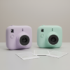 Two pastel instant film cameras with instant prints on a tabletop